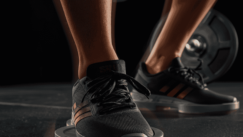 Dumbbell Squat Advanced Technique Spotlight: By placing small weight plates under the heels, trainees with limited ankle mobility can achieve a deeper squat depth.