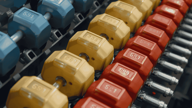 A close-up shot of neatly arranged dumbbell racks in a gym, showcasing various sizes of rubber hexagonal dumbbells ranging from light to heavy weights.
